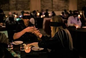 Gäste mit Augenbinden essen und trinken in einem abgedunkelten Restaurant