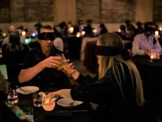 Gäste mit Augenbinden essen und trinken in einem abgedunkelten Restaurant