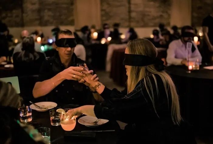 Gäste mit Augenbinden essen und trinken in einem abgedunkelten Restaurant