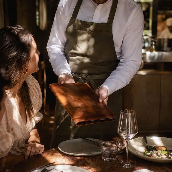 Gast betrachtet eine Speisekarte, die ein Kellner am gedeckten Tisch präsentiert